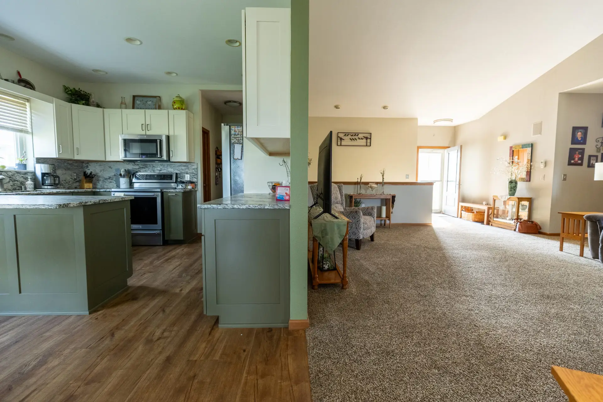 Split photo down a wall line. Fond du Lac home with a kitchen with LVP flooring (left), living room with carpet flooring (right)